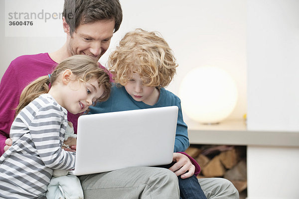 Nahaufnahme eines Mannes  der seinem Sohn und seiner Tochter bei der Benutzung eines Laptops hilft.