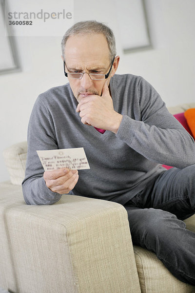 Mann  der beim Lesen einer Postkarte ernsthaft aussieht