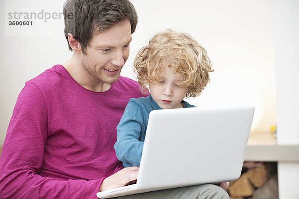 Nahaufnahme eines Mannes  der seinem Sohn bei der Benutzung eines Laptops hilft.