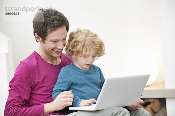 Nahaufnahme eines Mannes  der seinem Sohn bei der Benutzung eines Laptops hilft.