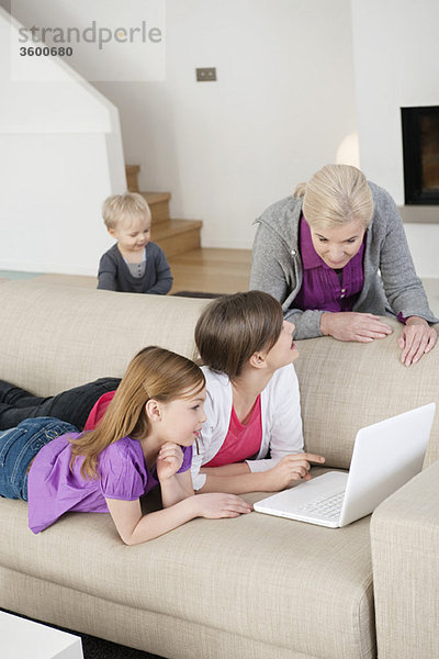 Zwei Mädchen  die mit ihrer Großmutter einen Laptop auf einer Couch benutzen.