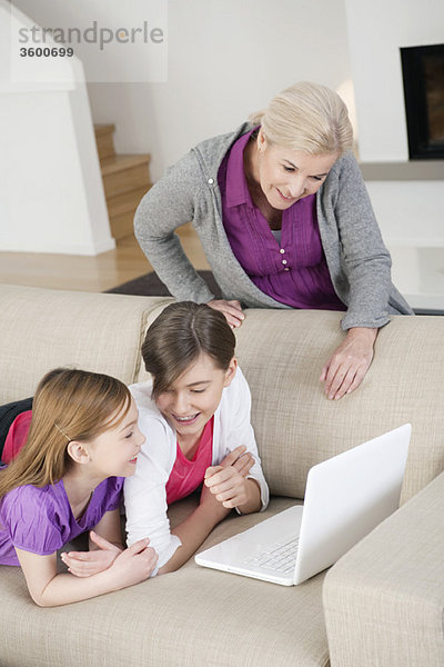 Zwei Mädchen  die mit ihrer Großmutter einen Laptop auf einer Couch benutzen.