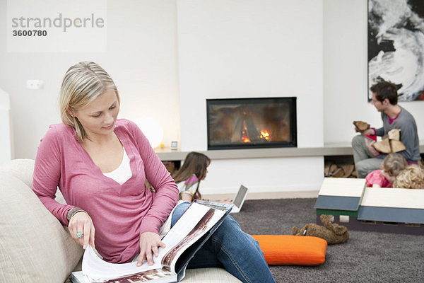 Frau beim Lesen einer Zeitschrift mit ihrer Familie im Wohnzimmer