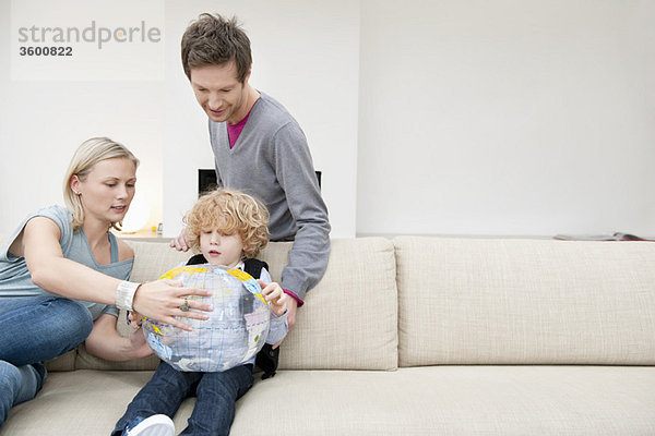 Eltern im Wohnzimmer mit ihrem Sohn  der einen Globus hält