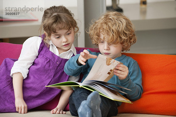 Junge sitzt mit seiner Schwester und liest ein Buch.