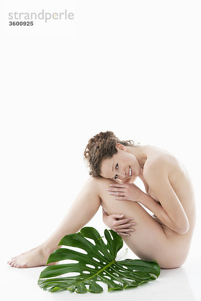Nackte Frau sitzend mit einem Philodendronblatt neben ihr