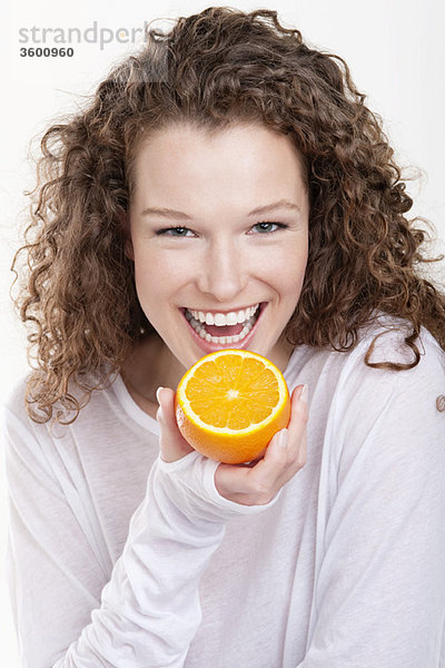 Porträt einer Frau  die eine halbe Orange hält und lacht