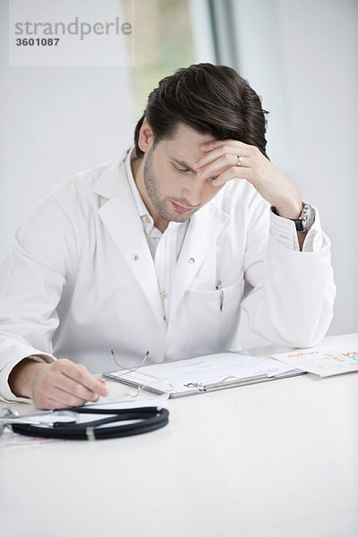 Ein männlicher Arzt untersucht einen medizinischen Bericht und sieht verärgert aus.