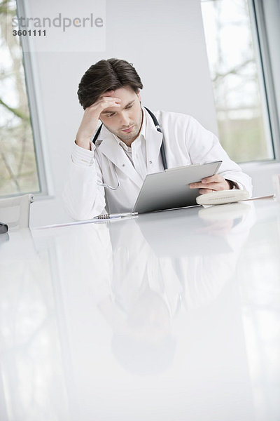 Ein männlicher Arzt untersucht einen medizinischen Bericht und sieht verärgert aus.