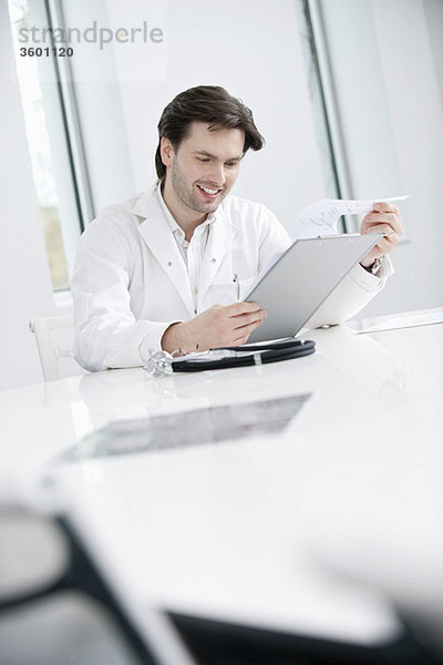 Ein männlicher Arzt  der einen medizinischen Bericht untersucht und lächelt.