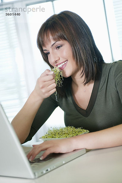 Geschäftsfrau  die Bohnensprossen isst und einen Laptop benutzt.