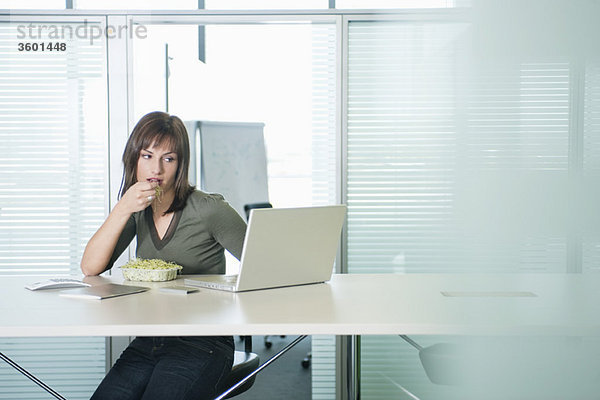 Geschäftsfrau  die Bohnensprossen isst und einen Laptop benutzt.