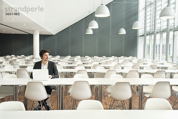 Geschäftsmann  der in einer Cafeteria sitzt und einen Laptop benutzt.