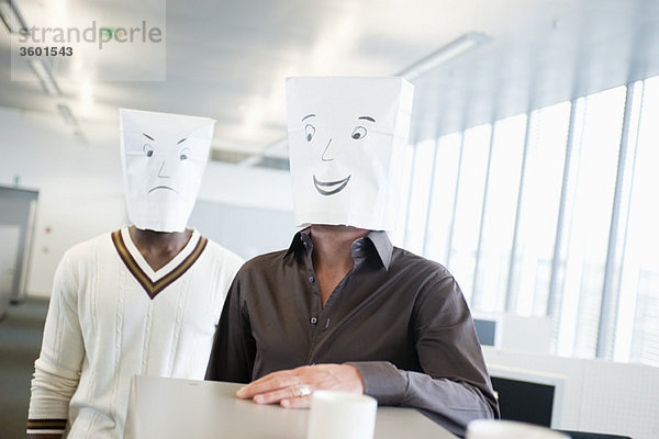 Zwei Geschäftsleute  die Papiertüten mit fröhlichen und traurigen Gesichtern tragen.