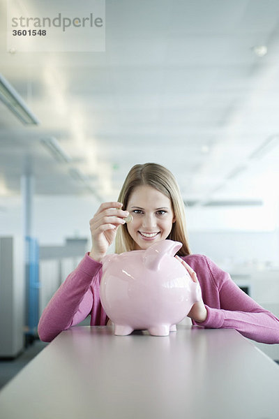 Geschäftsfrau beim Einwerfen einer Münze in ein Sparschwein