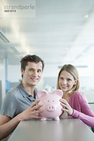 Geschäftsleute  die ein Sparschwein halten und lächeln