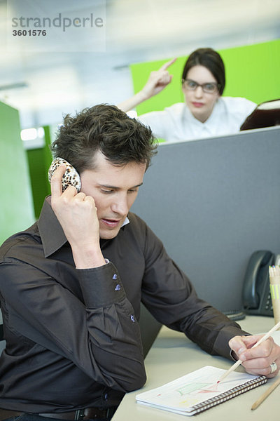 Geschäftsleute sprechen auf dem Handy  während sein Kollege wütend aussieht.