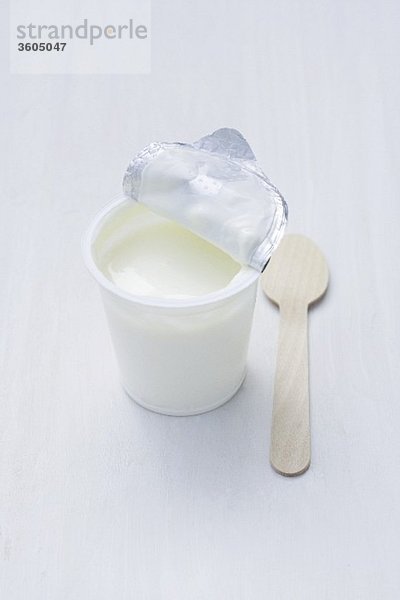 Joghurt im geöffneten Becher  daneben Holzlöffel
