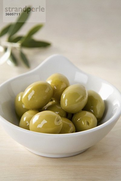 Grüne Oliven im Schälchen vor Olivenzweig