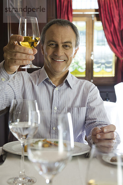 Ein reifer Mann  der ein Glas Wein zum Feiern aufzieht.