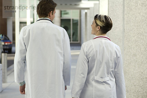 Ärzte beim gemeinsamen Plaudern und Gehen entlang des Krankenhausflurs  Rückansicht