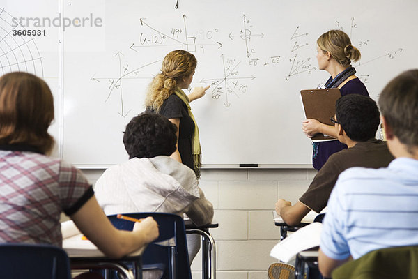 Lehrer hilft Schüler mit mathematischer Gleichung auf Whiteboard geschrieben
