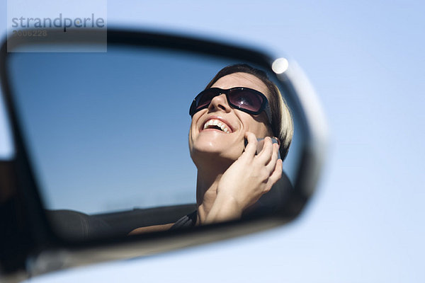 Frau spricht auf dem Handy  Spiegelung im Seitenspiegel