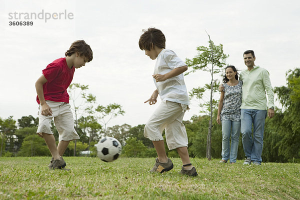 Jungen spielen Fußball  Eltern sehen im Hintergrund zu.
