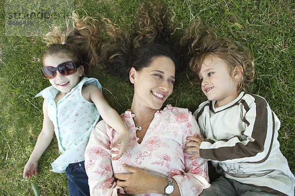 Mutter auf Gras liegend mit kleinen Kindern