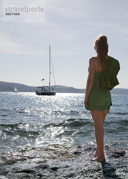 Frau am Strand mit Blick auf die Yacht