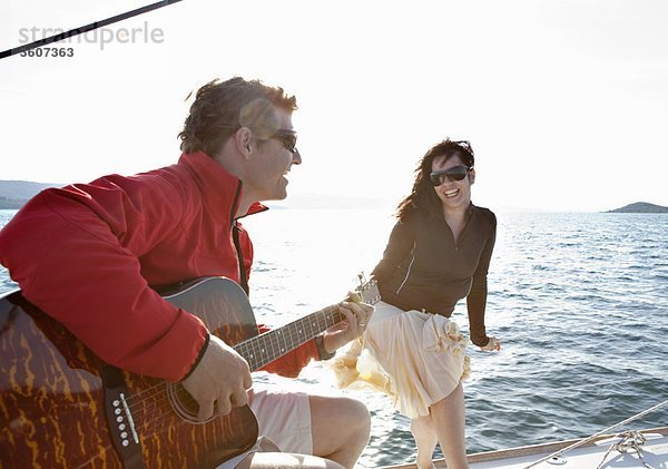 Frau und Mann spielen Gitarre auf der Yacht