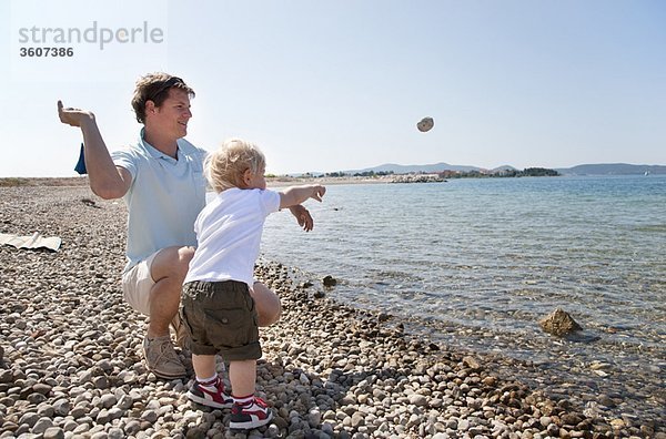 Vater und Sohn werfen Steine auf den Strand