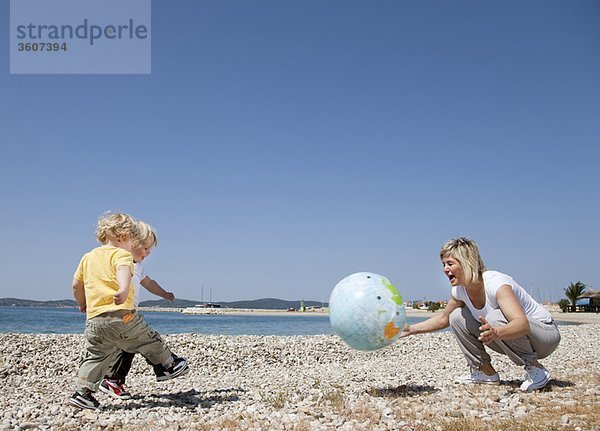 Mutter mit Zwillingen am Strand beim Ballspielen