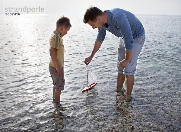 Vater und Sohn mit Spielzeugboot am Strand