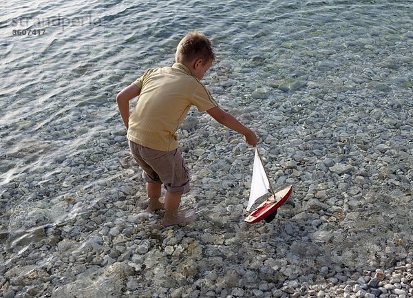 Junge mit Spielzeugboot am Strand