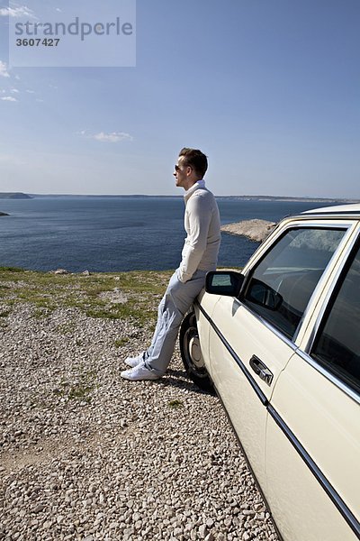 Mann mit Oldtimer mit Blick aufs Meer