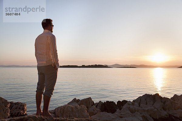 Mann beobachtet Sonnenuntergang am felsigen Strand