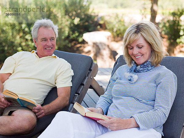 Erwachsene Paare lesen auf Liegestühlen im Garten