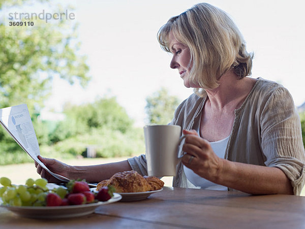 Frau im Freien mit Frühstück und Zeitung