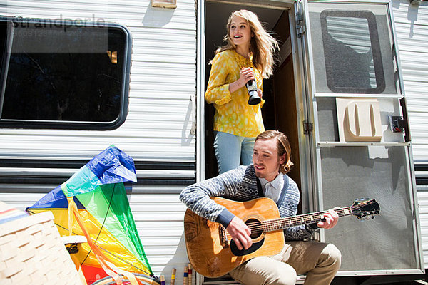 Junges Paar im Wohnwagen mit Gitarre und Videokamera