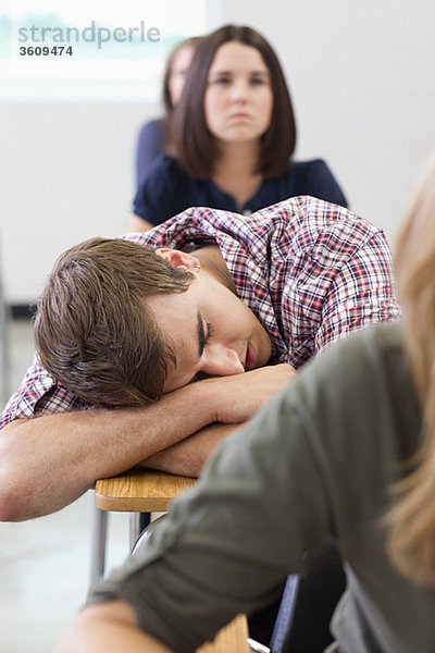 Männlicher Gymnasiast schläft in der Klasse