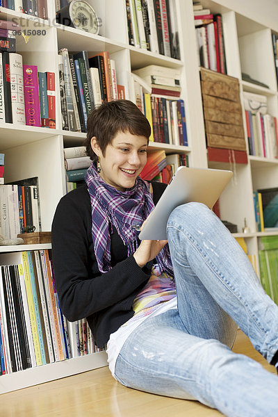 Junge Frau benutzt einen iPad vor einem Bücherregal