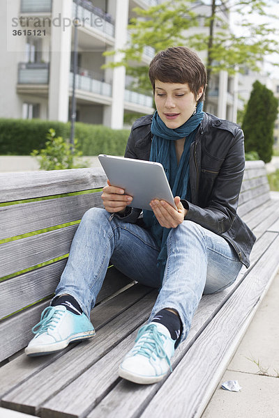 Junge Frau benutzt einen iPad auf einer Bank