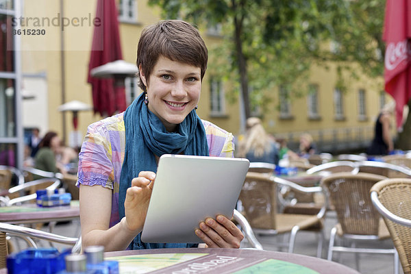 Junge Frau benutzt einen iPad in einem Straßencafe