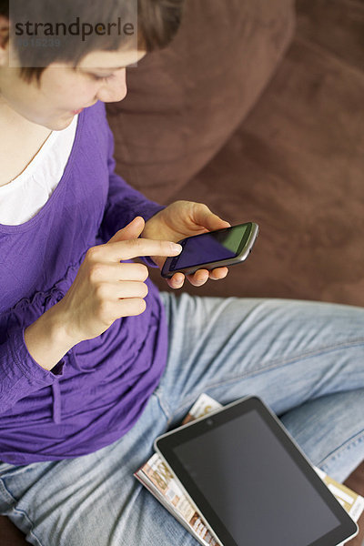 Junge Frau mit Smartphone und iPad auf der Couch
