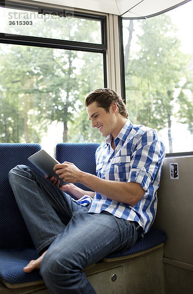 Junger Mann benutzt einen iPad in der Straßenbahn