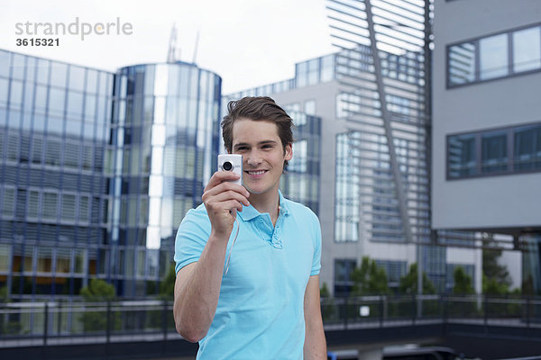 Junger Mann mit Smartphone vor einem Bürogebäude