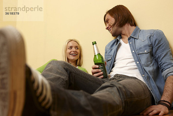 Junges Paar sitzt auf dem Fußboden und trinkt Bier