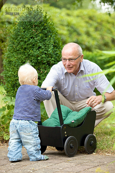 Großvater und Kleinkind mit Puppenwagen im Freien