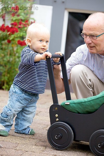 Großvater und Kleinkind mit Puppenwagen im Freien